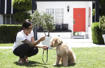Woman crouching outdoors, smiling, holding a dog attached to a leash
